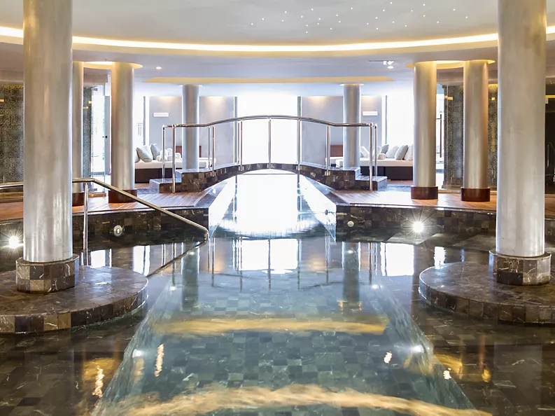 An indoor pool at the spa in the luxury hotel with pillars in the water and comfortable seating in the background.