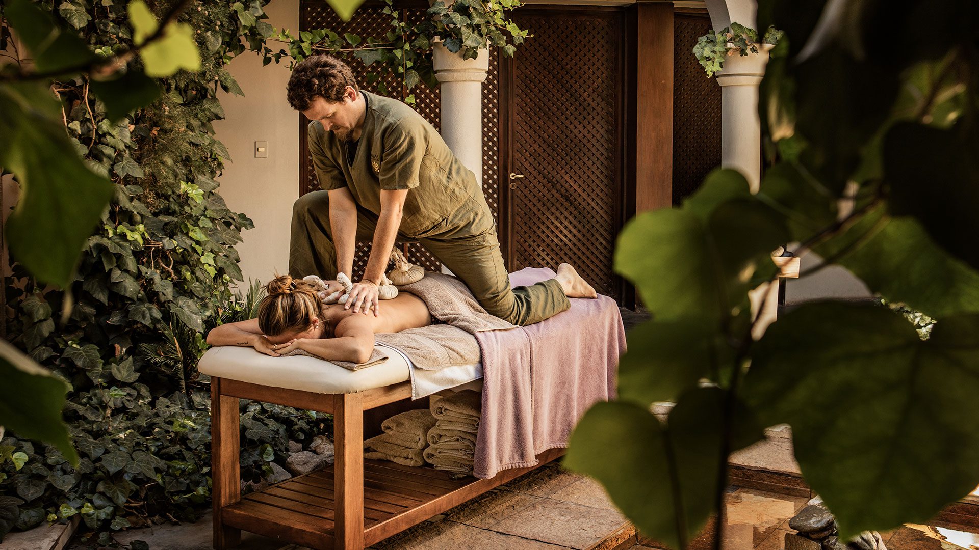 A woman receiving a massage outside surrounded by lush greenery.