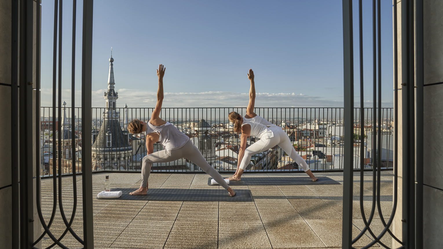 Two women enjoying yoga on a terrace at the luxury hotel, overlooking the incredible Madrid skyline.