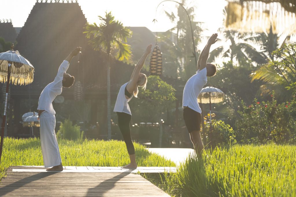 A serene scene of three people engaged in yoga on vibrant grass outside of the Alaya Resort, radiating luxury and connection with the natural world.