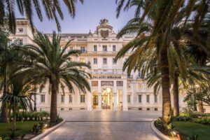 The entrance of the luxury hotel. The path lined by plants and trees on either side, leading to the incredible front of the Gran Hotel Miramar.