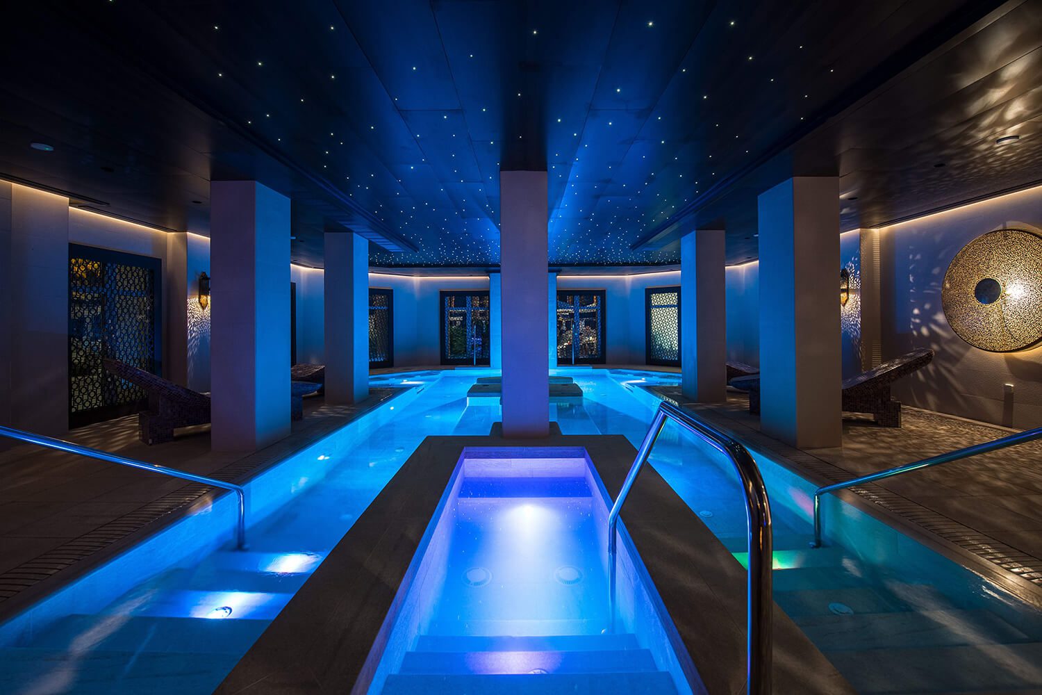 An indoor pool at the luxury hotel with loungers along the edge of the pool and dim lights for relaxation.