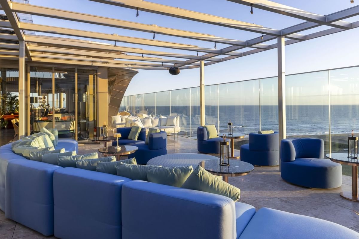 A variety of blue outdoor sofas and chairs and small tables, complete with a view of the beach.