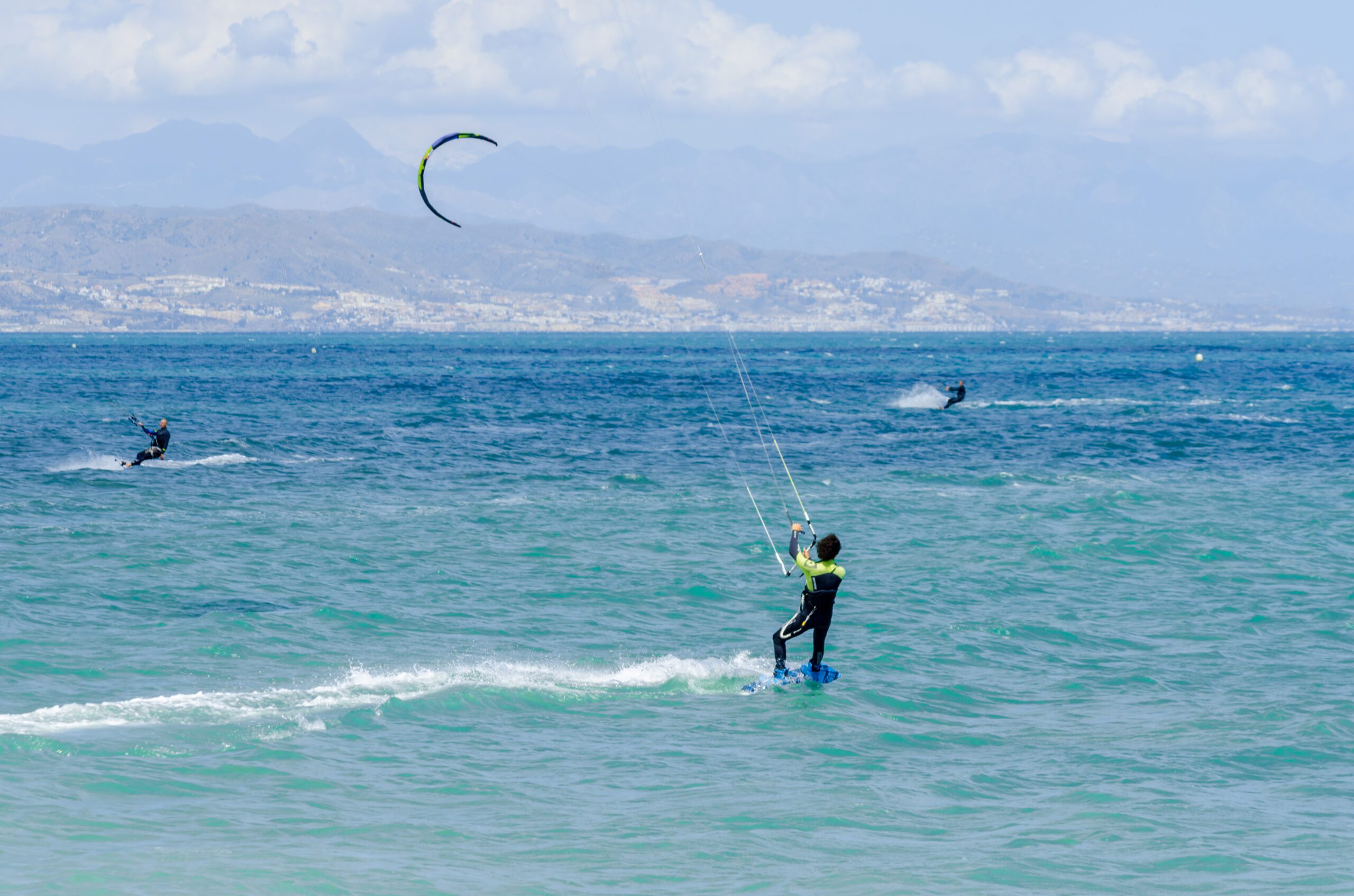 Two kite surfers in the distance with their kites up in pale blue skies with fluffy clouds in Malaga Andalucia Spain