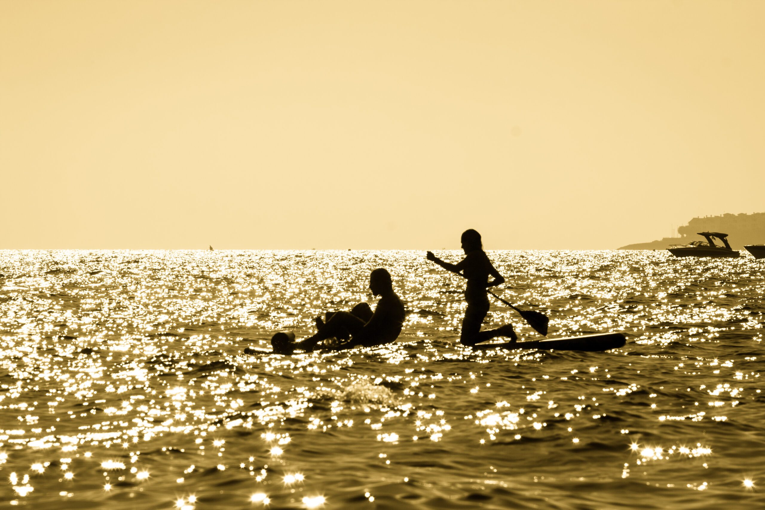 Silhouette of two people paddling out to sea on paddle boards at Maro beach in Malaga Spain at sunset with the sky and sea stained a yellow or orange colour from the sun setting