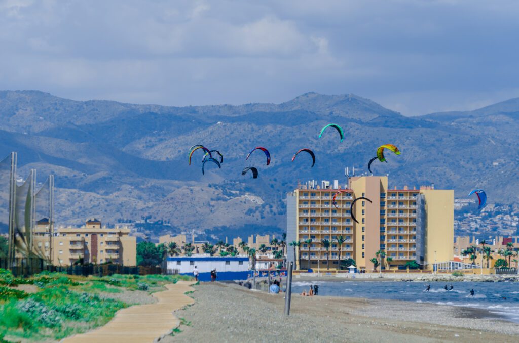 Many kitesurfer kites in the sky with apartment blocks andthe mountains in the background on a windy cloudy day in Malaga Spain