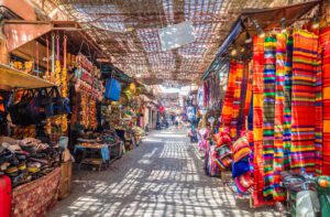 A view through the Djemaa el Fna market with vibrant clothes and souvenirs on either side of the path.