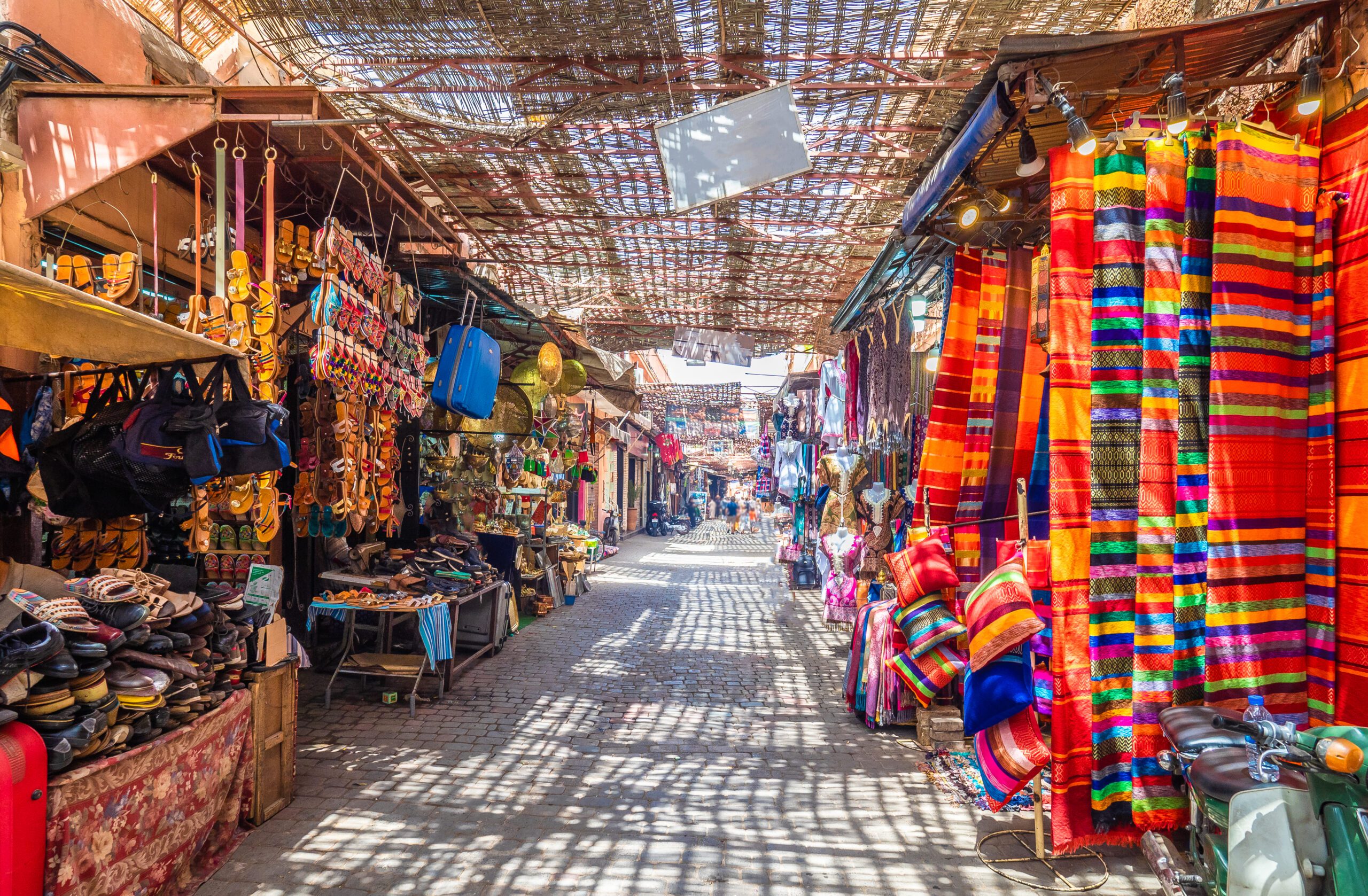 A view through the Djemaa el Fna market with vibrant clothes and souvenirs on either side of the path.