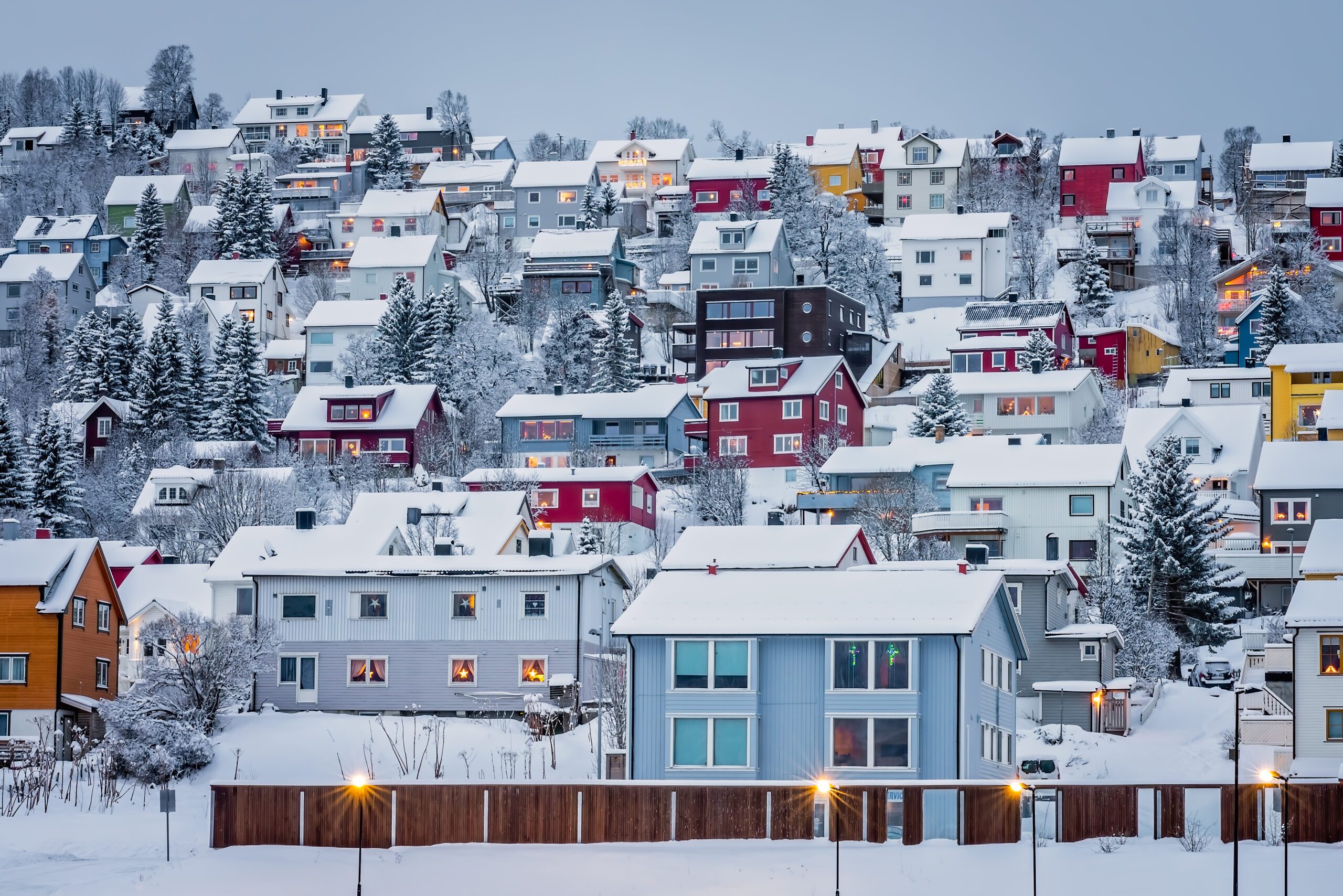 Pastel blue, white and red coloured hillside houses in Tromso Norway with snowy roofs.