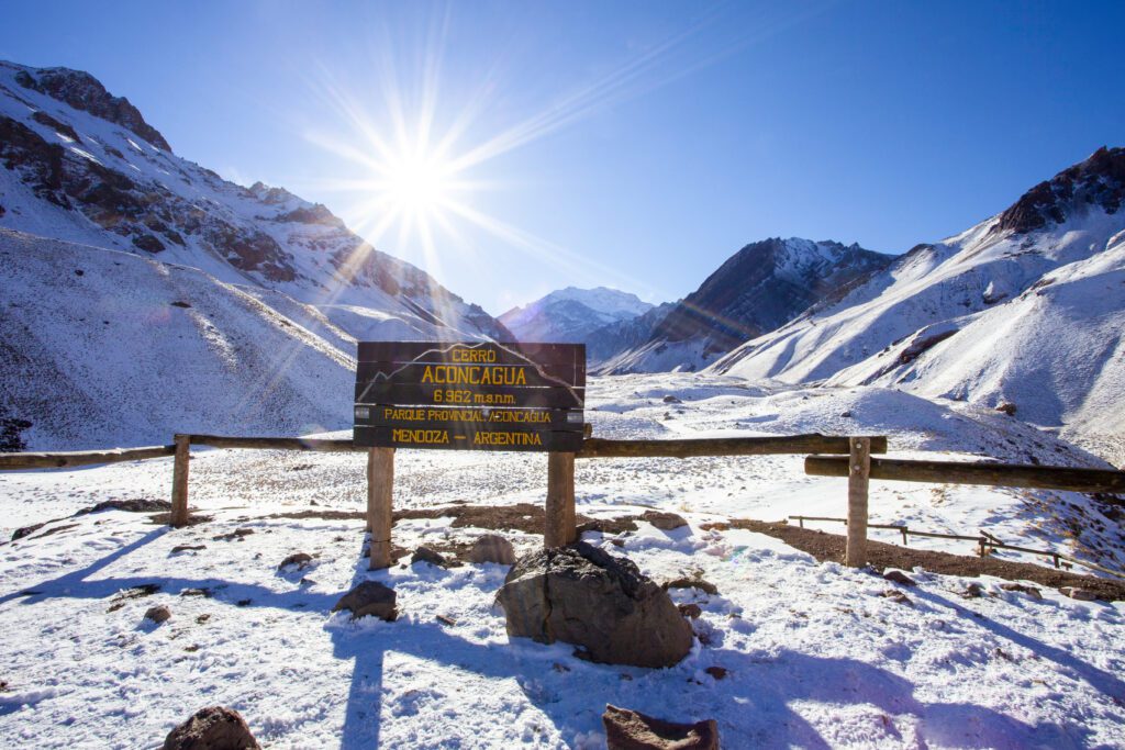 Sign showing the entrance to the Aconcagua Provinical Park in Mendoza Argentina with snowy mountains and a clear blue sky with the sun glistening