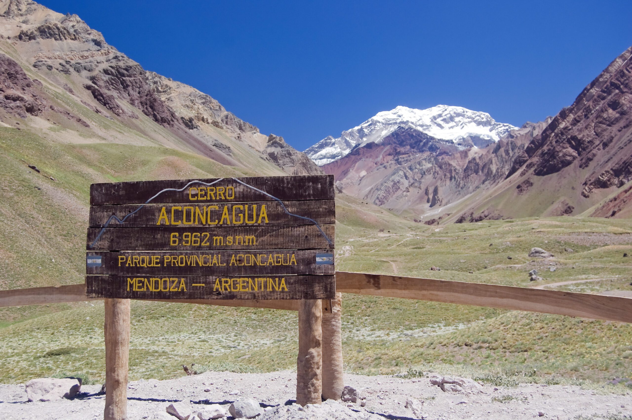 A sign at the entrance to the Aconcagua Provincial Park with views of the mountains and trail in the background.