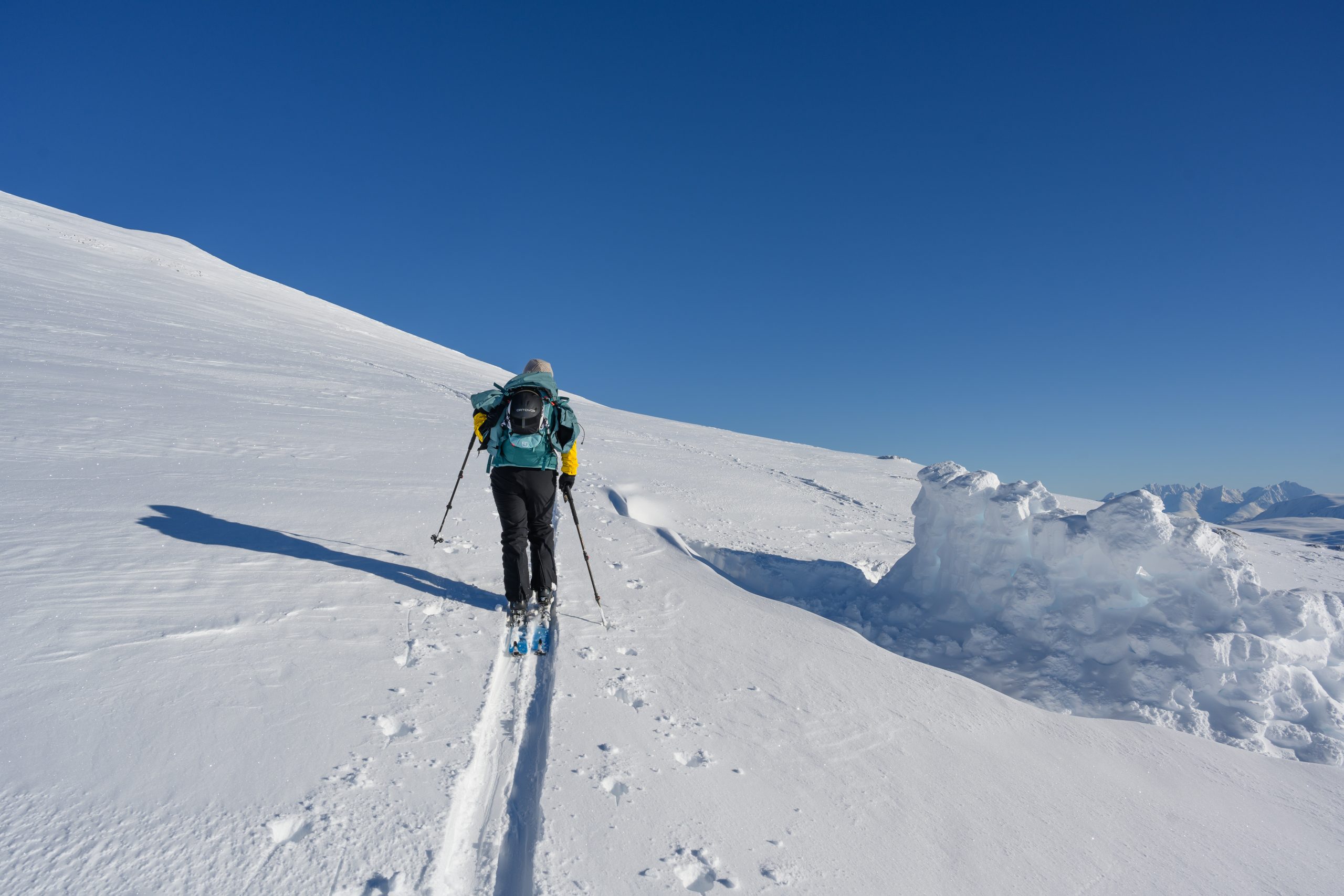 Solo travllers on a ski tour in Tromso Norway leaving tracks behind in untouched fresh snow with a deep blue sky.