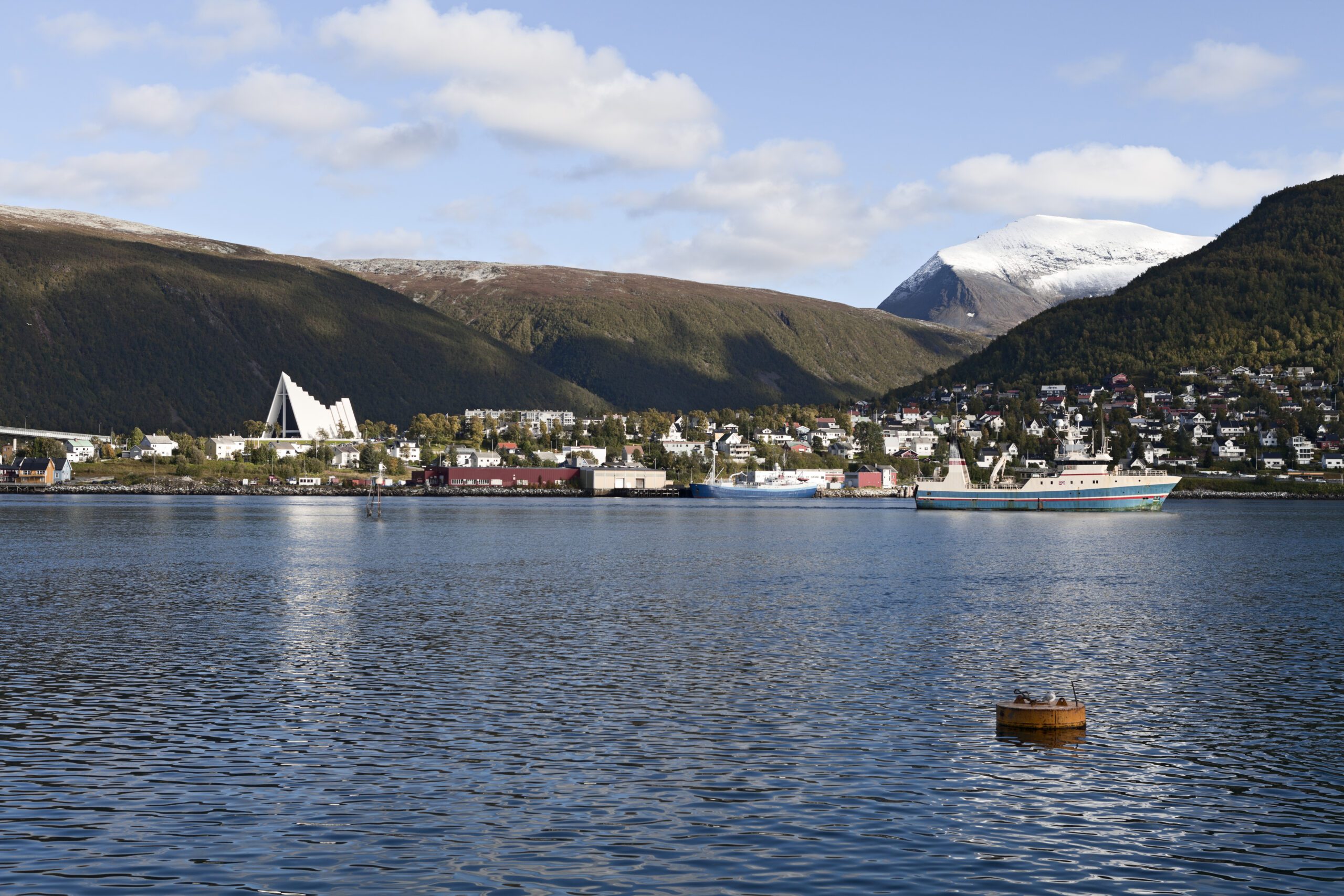 View over the water toward the East side of the city of Tromso in Norway with calm waters and pale blue sky