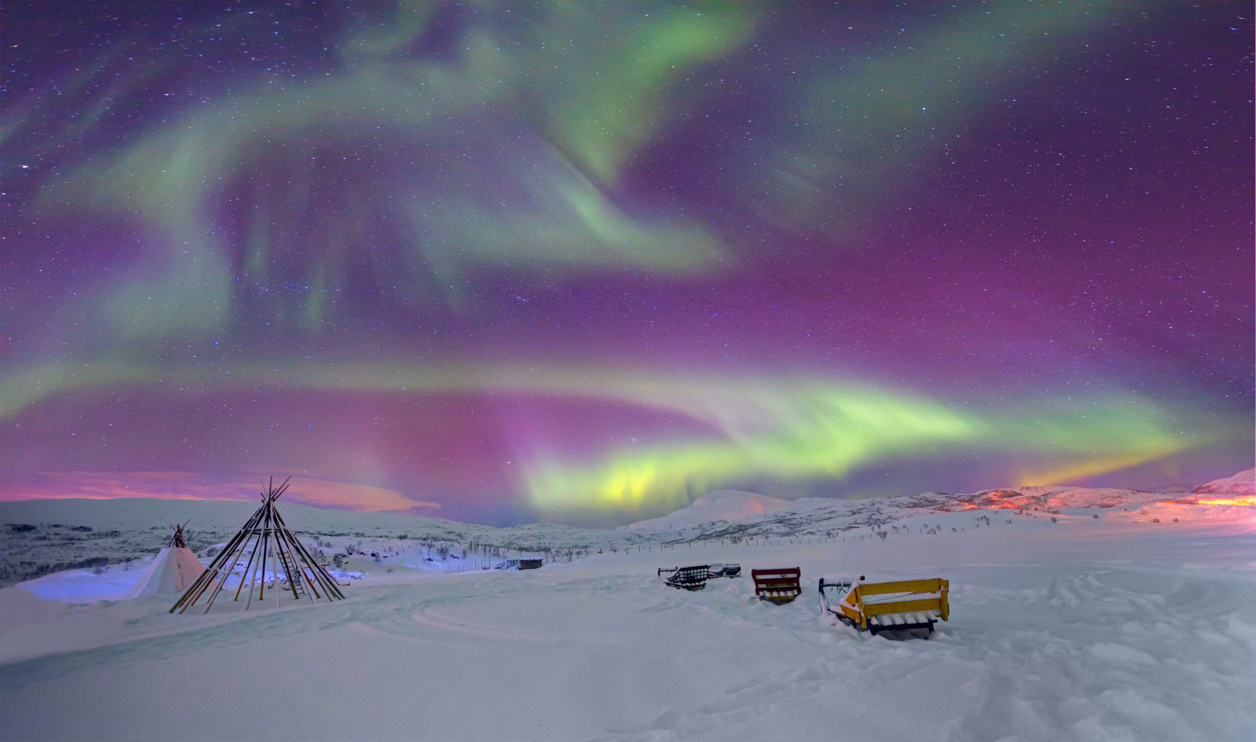 Northern lights or Aurora borealis in the sky over Tromso, Norway. the sky is lit up purple and pink with fluorescent green swirls. Snow on the ground.