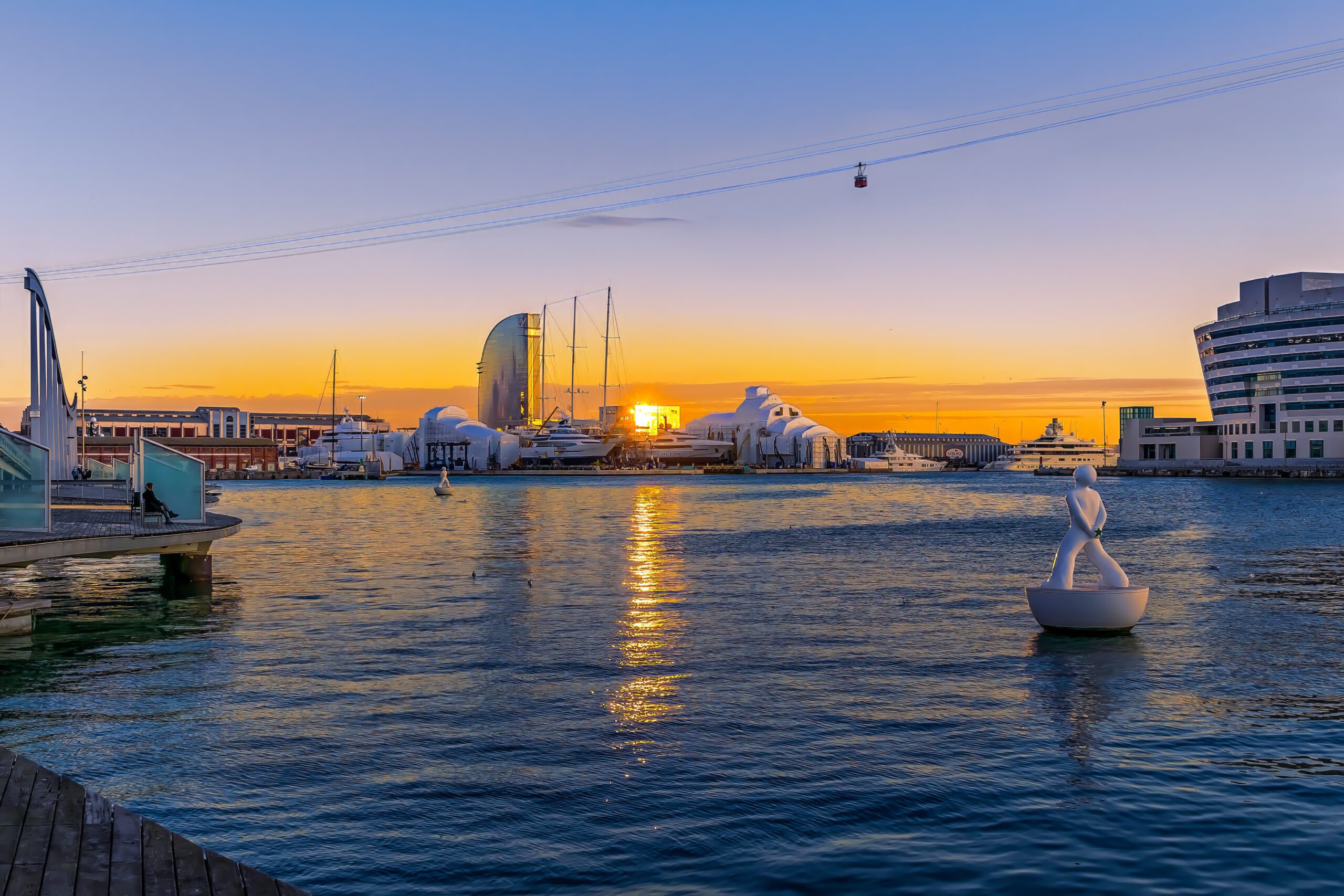 Golden sunset sun reflected in the waters of the Mediterranean Sea in the evening at Port Vell in Barcelona. Seascape with cable car and Hotel W Barcelona at dusk