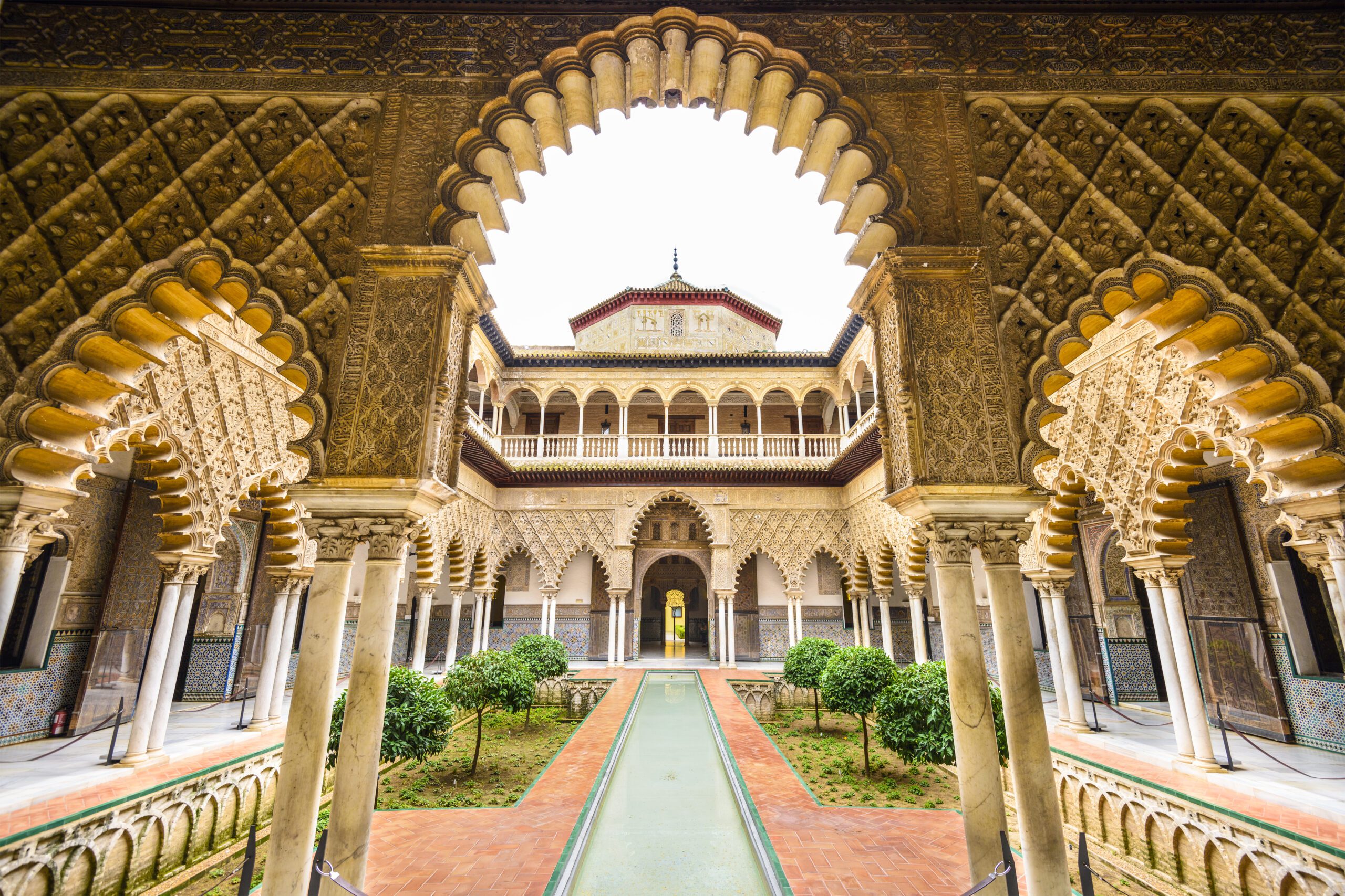 View through the arches of the Royal Alcazar of Seville. Ornate archways with a long water feature pond running throuogh the centre courtyard.