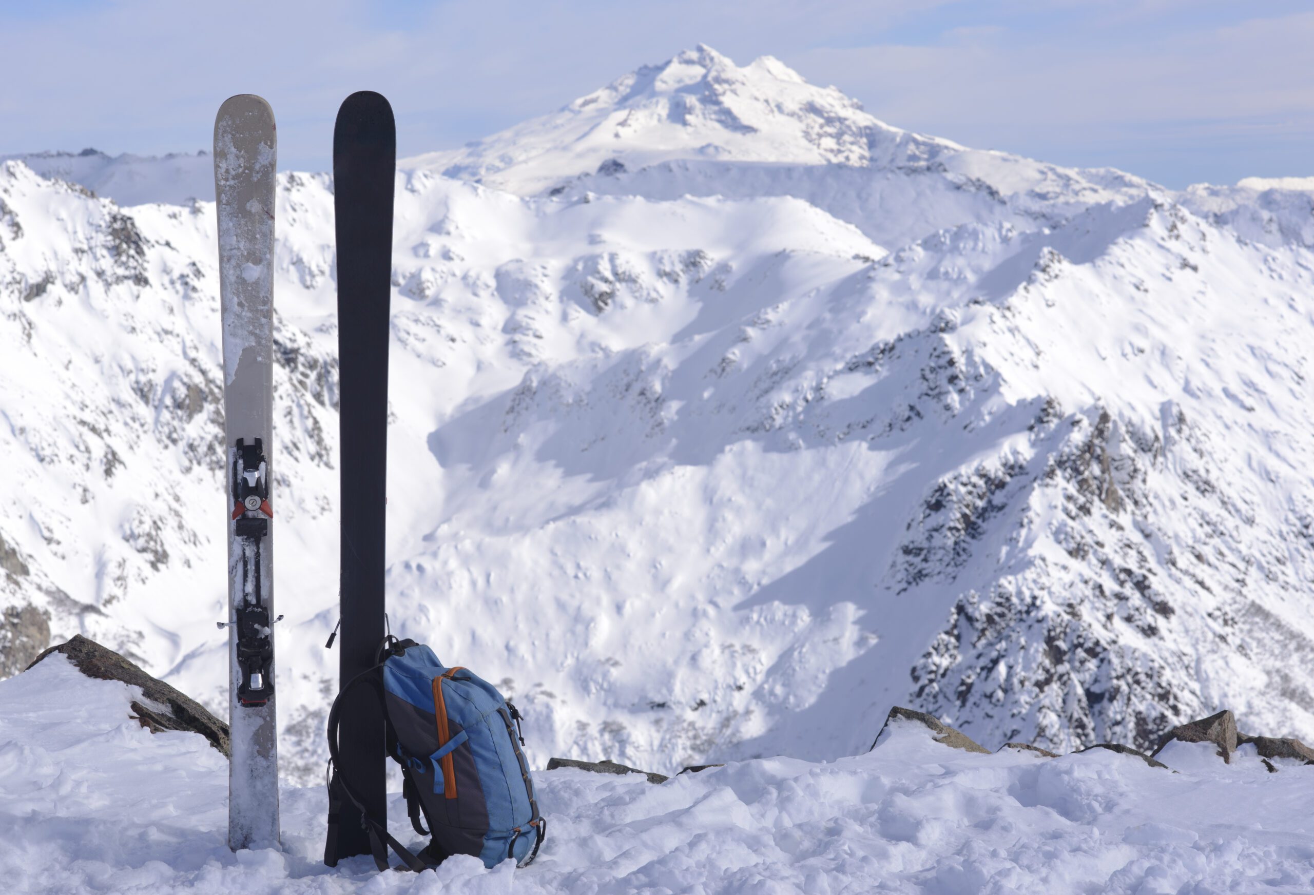 Pair of skis planted upright in the snow with a back pack leaning aginst them with a snowy backdrop of mountains behind