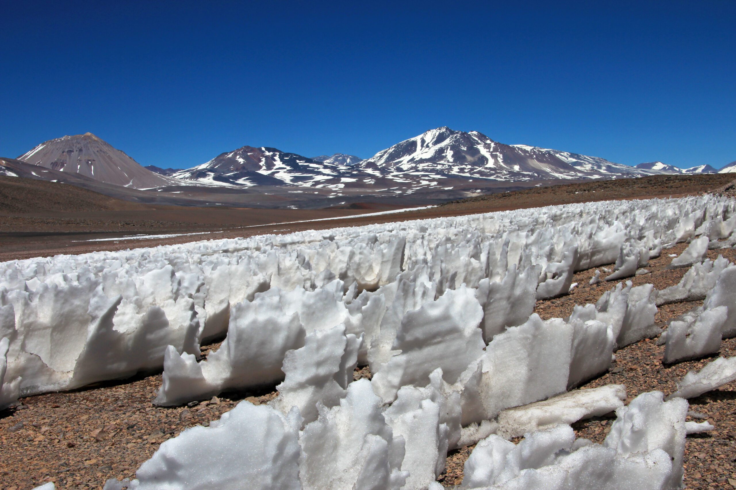 Multiple ice or snow formations standing upright in a large sharp crystal type of shape on the barren ground with Ice capped mountains behind in Penitentes Mendoza on the border with Chile