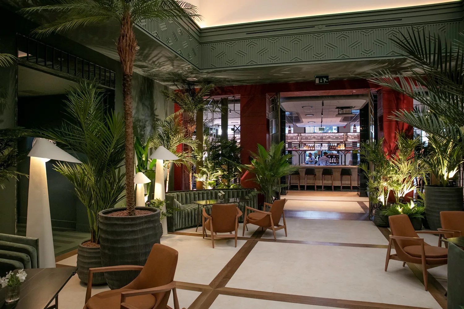 The lobby at the luxury hotel, featuring an array of tables, chairs and a variety of potted plants.