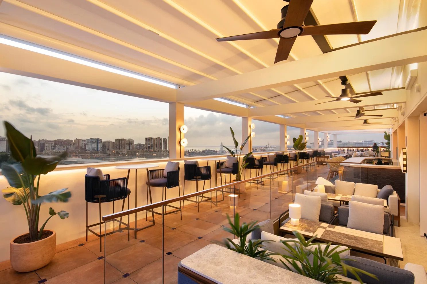 A dining area at the luxury hotel , featuring a variety of chairs, tables and potted plants, complete with large windows displaying the incredible views of Málaga.