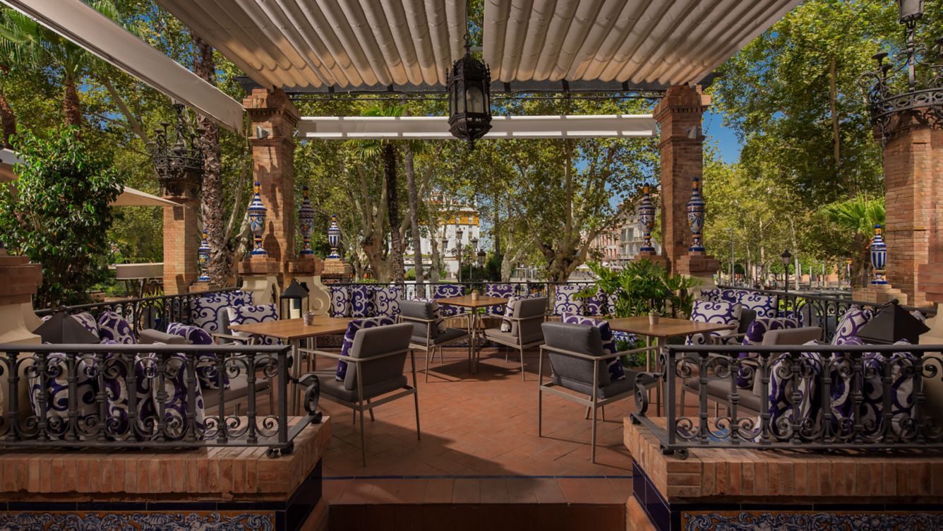 A dining area outside the luxury Hotel Alfonso XIII with a few tables and chairs, surrounded by lush greenery.