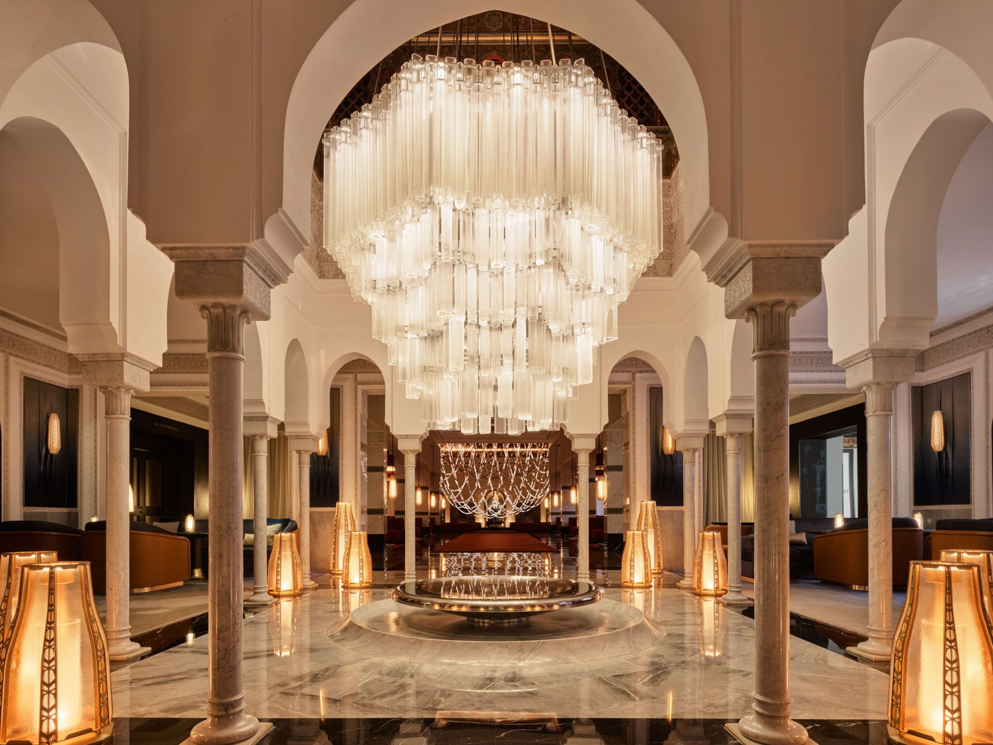 Lavish hotel lobby with magnificent pillars and marble floors, the ceiling adorned with a sparkling chandelier.