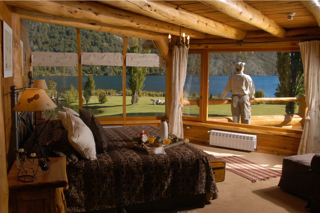 A bedroom at the luxury hotel, showing the large bed, rustic interior and incredible view of the lake and mountains outside.