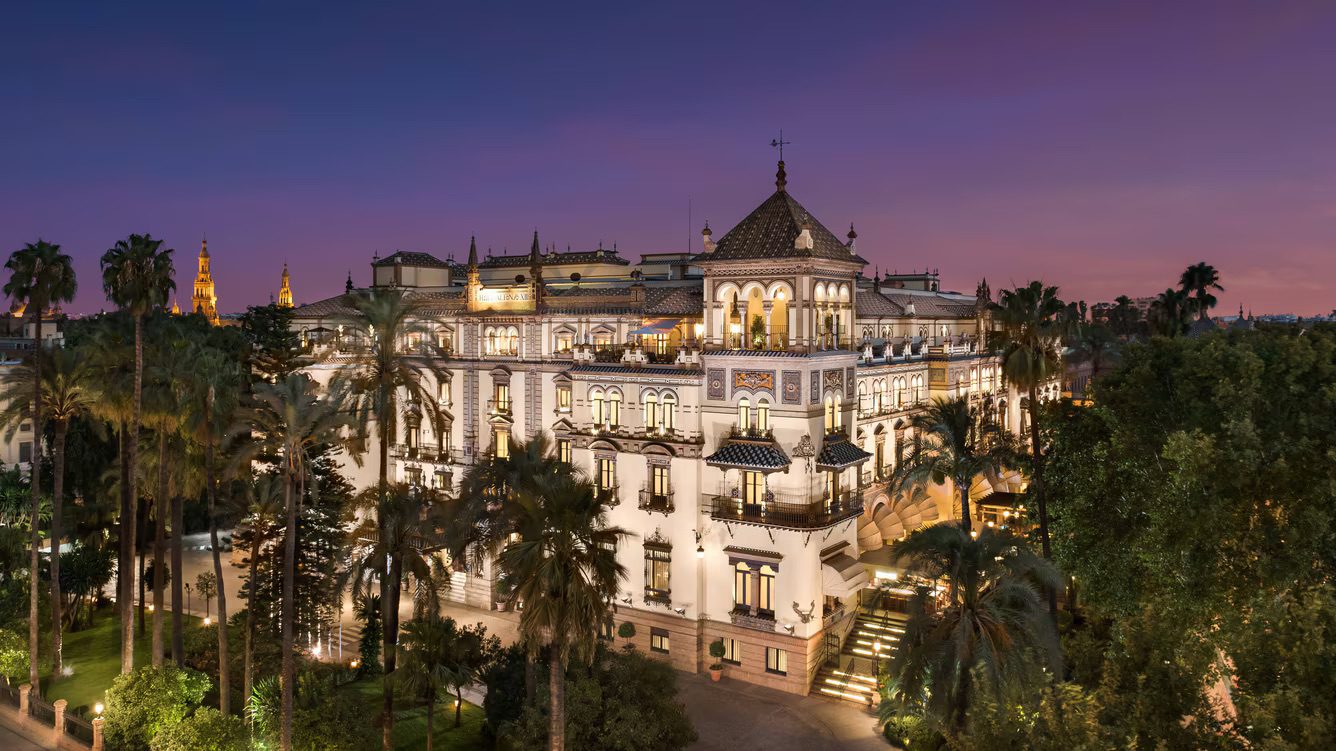 A view of the luxury Hotel Alfonso XIII surrounded by towering trees and an incredible sunset in the background.