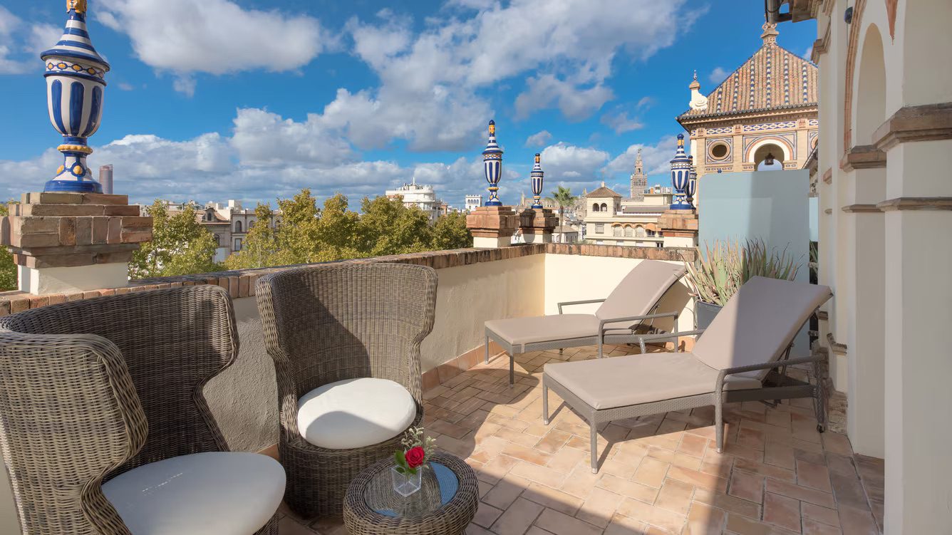 A private balcony at the luxury Hotel Alfonso XIII with two chairs, two sun loungers, a small table, all complete with incredible views of Seville.