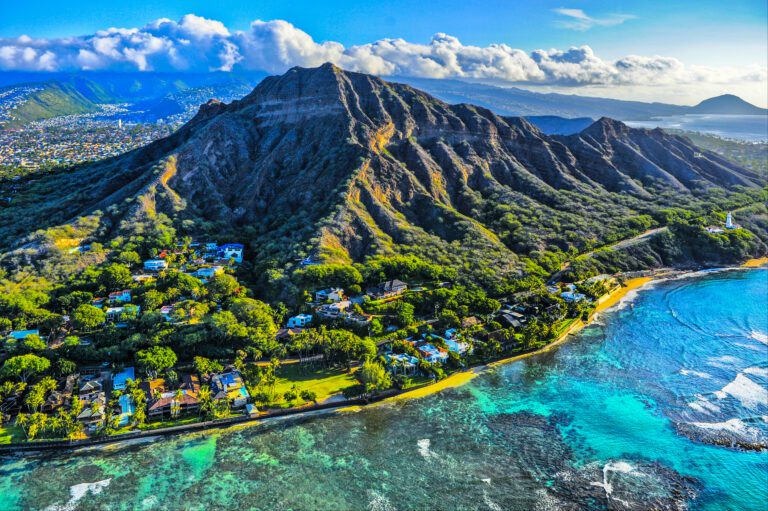 IMage of the diamond crater in Honolulu in Hawaii where the luxury properties are at the base of the rocks rolling into the shore and the crystaln clear waters with the waves lapping over the shallow rocks