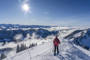 Woman snowshoeing along a ridge with a sea fog below her with the caps of a mountain range poking throug. Stunning blue sky with bright sunlight.