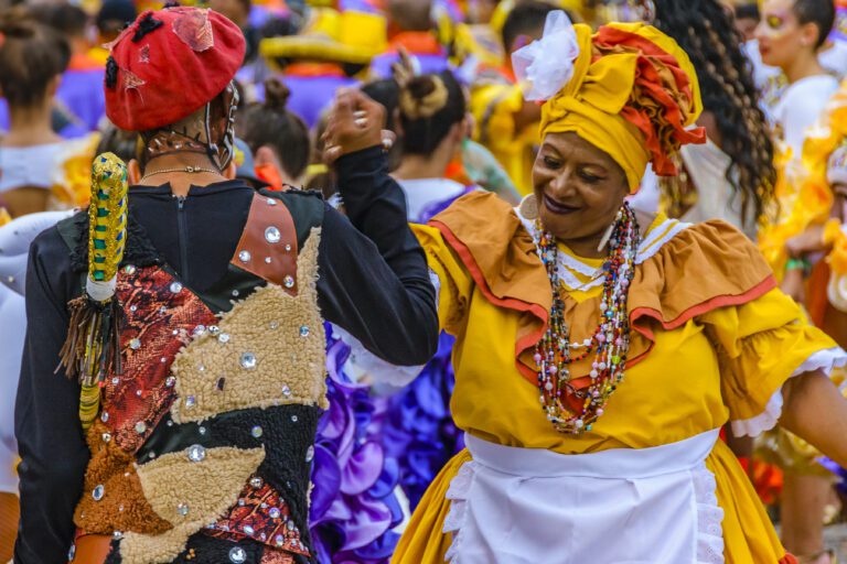 Image of a group of Candombe women dancers dressed in traditional costume that are bright yellow, red, purple and white waiting to join the street parade at the Montevideo Carnival in Uruguay.