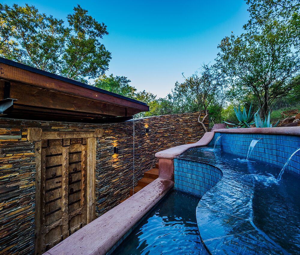 An outdoor pool surrounded by greenery and blue skies above.