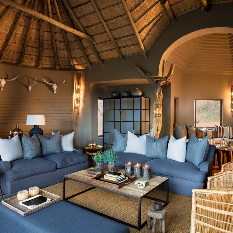 A living room in the safari lodge with an array of comfortable blue couches, a table in the middle and warm lights lighting up the room.