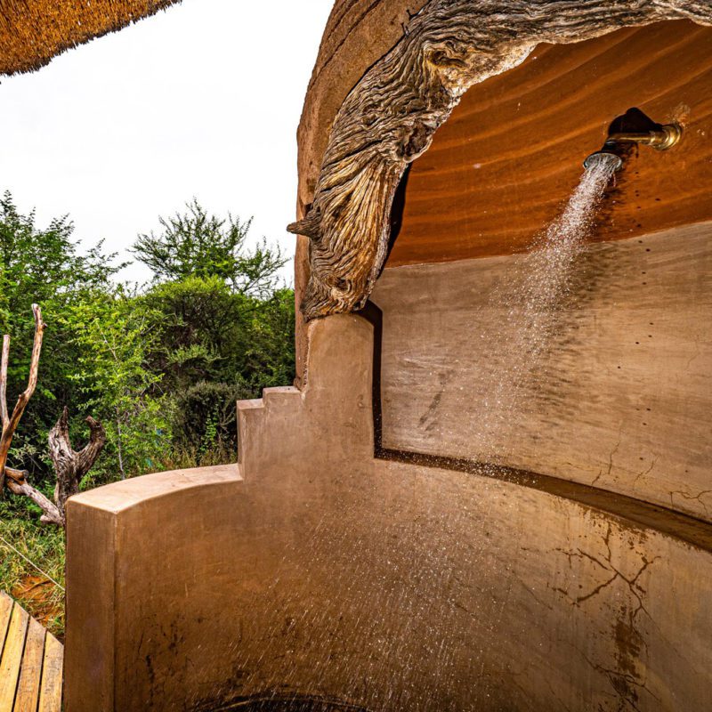 A luxury outdoor shower with stone walls and views over the safari's greenery