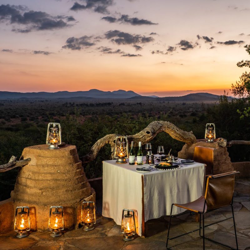 A table set for one overlooking the African landscape and sunset with candles lit around the table.