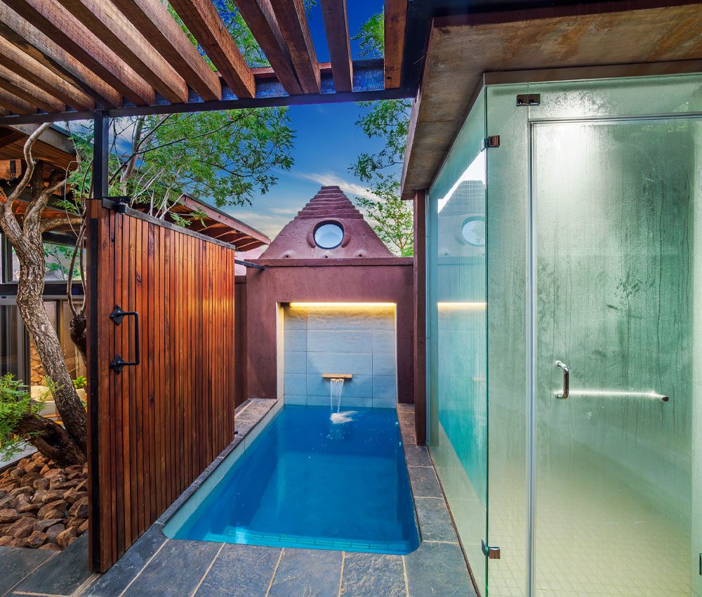 An outdoor pool and steam room with blue sky and trees behind.