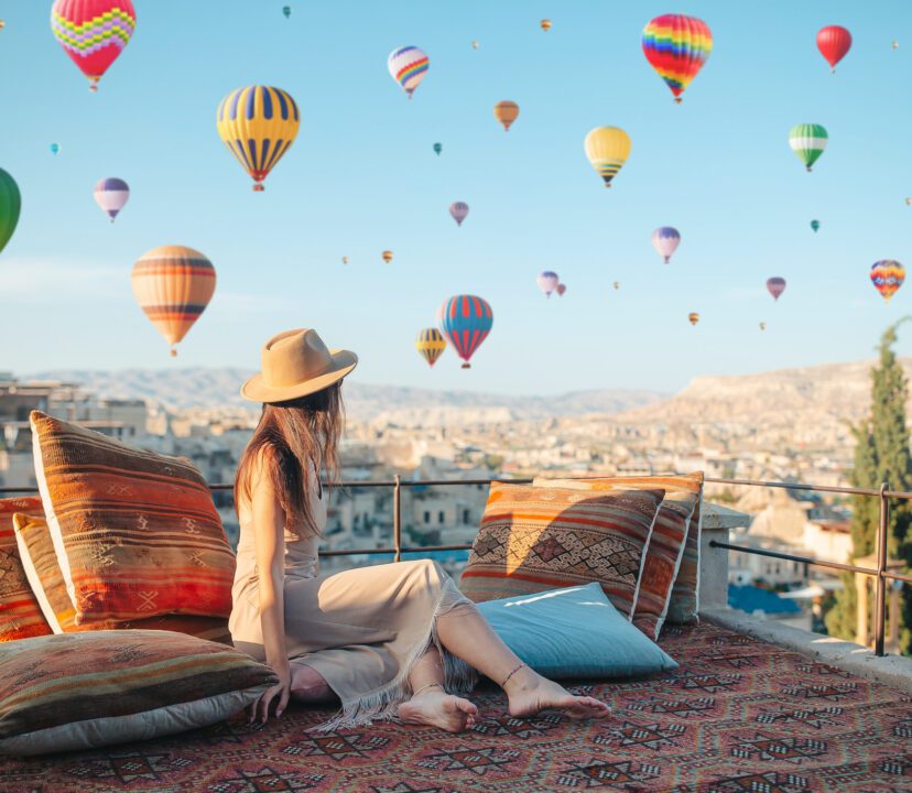 Young woman travelling solo in Cappadocia. Woman on a rooftop with air balloons in Goreme in Cappadocia, Turkey