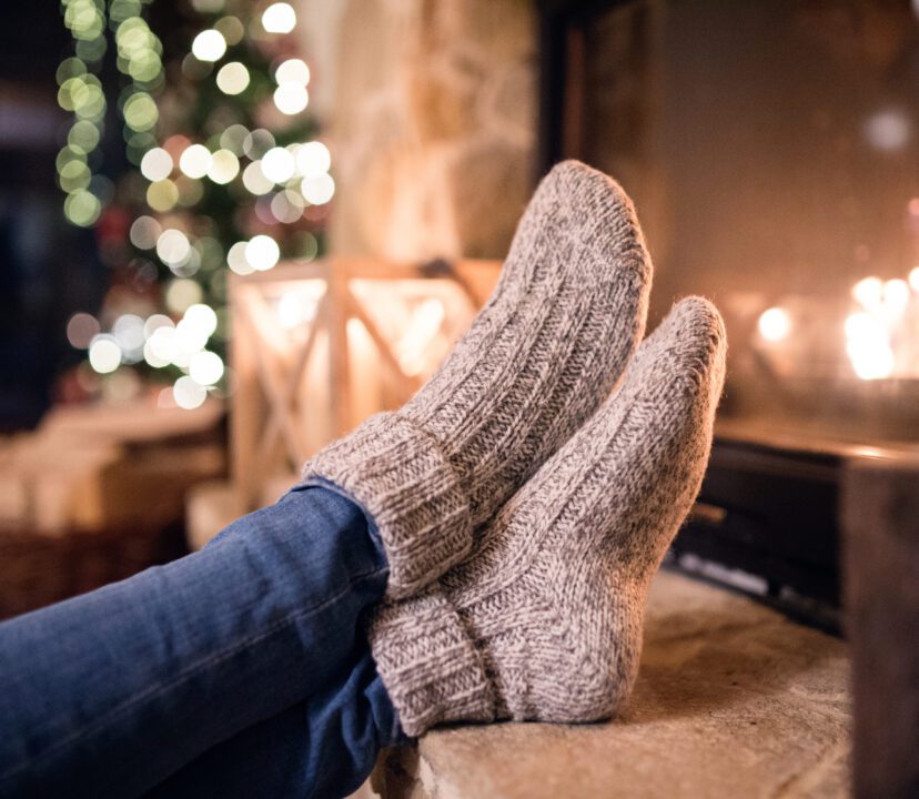 Solo female is sat by a fire at Christmas Time - warming her feet in cosy socks