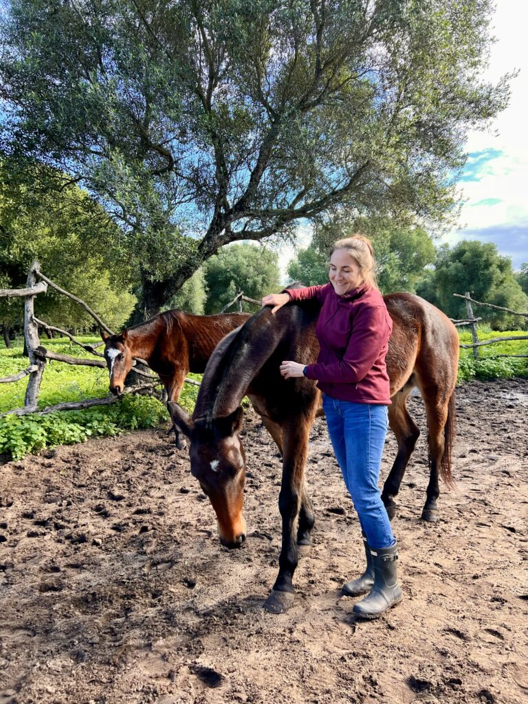 Clare Westwood from Travel with Abeona smiling with one of the coaching horses and another horse behind