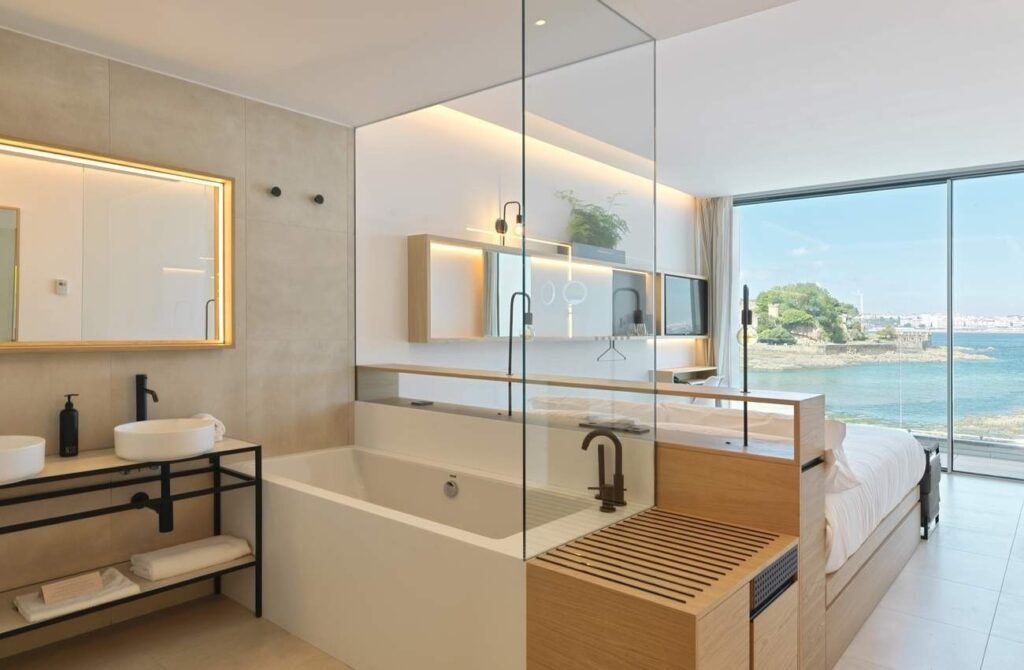 A bedroom in the luxury hotel featuring a sink, bathtub bed and large windows opening onto a private balcony.
