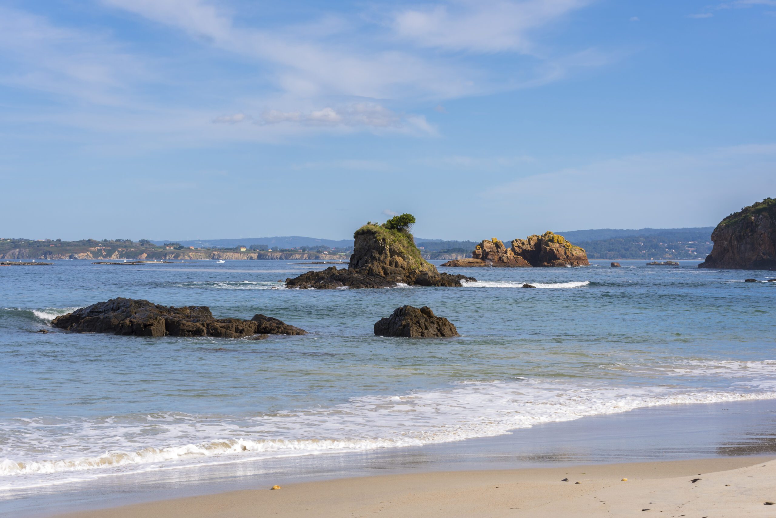 A beach in A Coruña, Spain, with rock structures emerging out of the clear ocean.