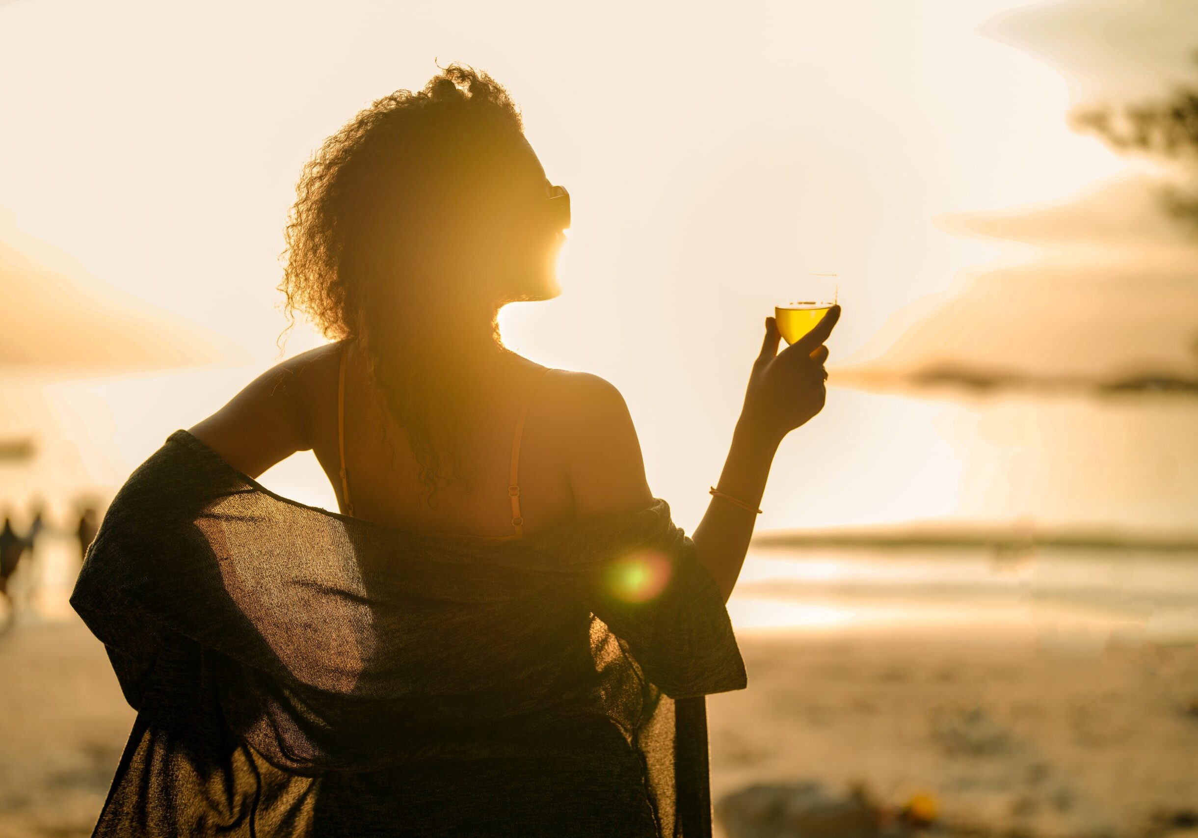 Woman enjoys a luxury solo female travel moment - looking wistfully at the sunset whilst enjoying a fabulous drink