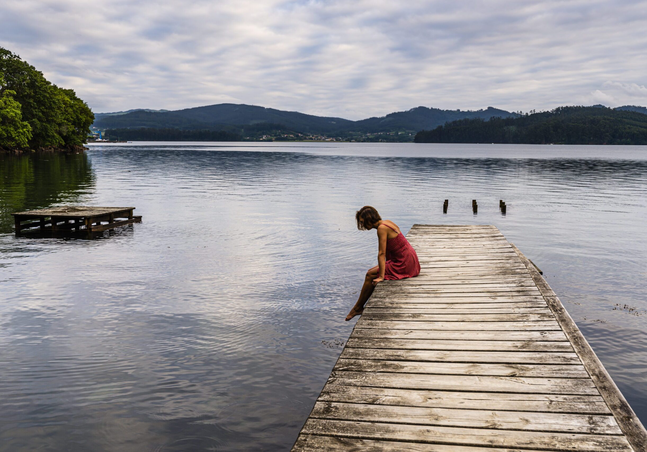 Woman sits on a pier looking down. Nerves abound when considering embarking on luxury travel alone.