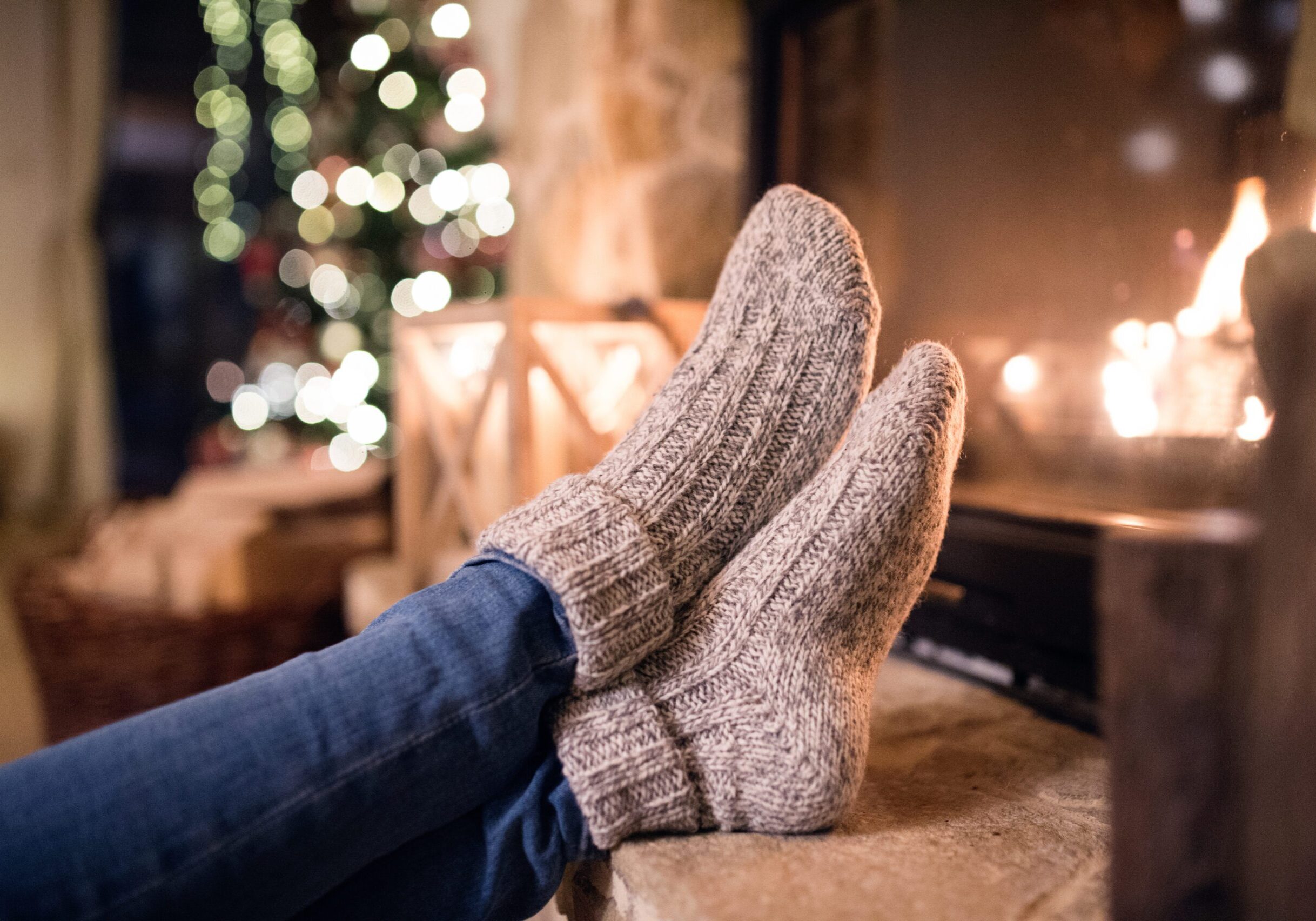 Solo female is sat by a fire at Christmas Time - warming her feet in cosy socks